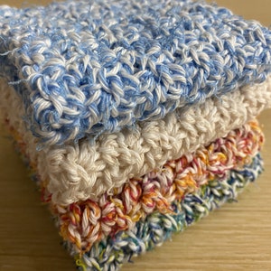 Może przedstawiać: Stos czterech dzianych ręczników kuchennych w różnych kolorach, w tym niebieskim, białym, pomarańczowym i zielonym.