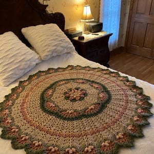 Peut inclure: Une couverture en crochet dans les tons de brun, vert et rose avec un motif circulaire. La couverture est sur un lit avec des oreillers blancs.
