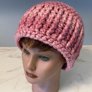 May include: A hand-knitted, pink beanie hat. The hat is made of thick yarn, with a ribbed texture. The color is a blend of light and dark pink hues. The hat is designed to be worn on the head, covering the ears and forehead.