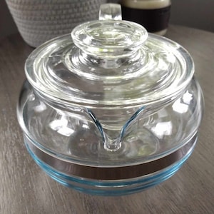 May include: A clear glass teapot with a blue and brown striped band around the bottom. The teapot has a lid and a spout.