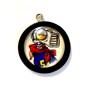 May include: A round black framed pendant with a cartoon image of a robot wearing a red bandana and a blue shirt with the number 5 on it. The robot has a large yellow eye and a silver body.