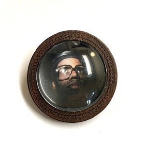 May include: A round, brown wooden frame with a glass insert. The frame contains a black and white photo of a person wearing glasses.