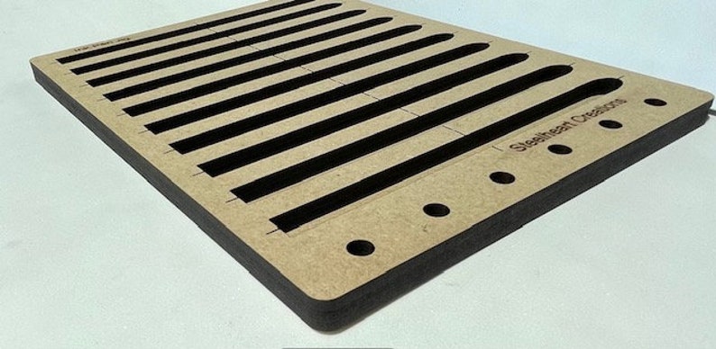 May include: A wooden craft board with 10 slots for making bracelets. The board is brown with black edges and has the text "Sleekheart Creations" printed on the bottom right corner.
