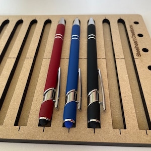 May include: Three pens in a wooden holder. The pens are red, blue, and black. The holder has the text "Steelheart Creations" on it.