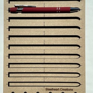 May include: A wooden jig with the text "Ink Pen Jig" and "Steelheart Creations" for holding and aligning ink pens. The jig has eight slots for pens and five holes along the bottom.