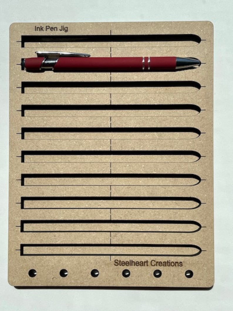 May include: A wooden jig with the text "Ink Pen Jig" and "Steelheart Creations" for holding and aligning ink pens. The jig has eight slots for pens and five holes along the bottom.