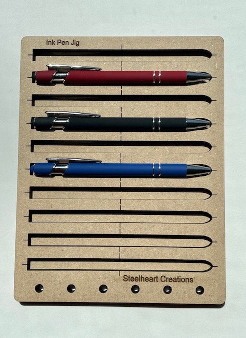 May include: A wooden jig with slots for holding ink pens. The jig has the text "Ink Pen Jig" and "Steelheart Creations" printed on it.