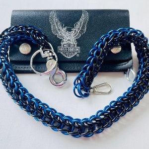 May include: A blue and black chainmail wallet chain with silver-tone clasps, displayed with a black leather wallet. The wallet features a Harley-Davidson logo. The chain is made of interwoven metal rings.