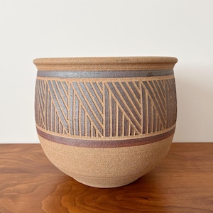 May include: A brown ceramic planter with a geometric pattern in shades of brown and gray. The planter has a rounded shape and a wide opening.