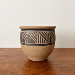 May include: A brown ceramic planter with a black geometric pattern around the middle.