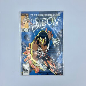 May include: Marvel's "The Falcon" comic book, issue #1 from a limited four-issue series. The cover shows the Falcon character in action, set against a blue and grey backdrop. The comic is protected in a clear sleeve.