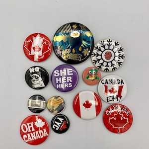 May include: A selection of circular badges with diverse designs. Many showcase the Canadian maple leaf emblem. Other badges display text such as "OH CANADA" and "CANADA EH!" alongside various graphics.