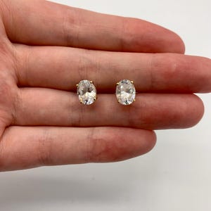Peut inclure: Une paire de boucles d'oreilles à clous de forme ovale avec des pierres transparentes à facettes serties dans des griffes en métal doré. Les boucles d'oreilles présentent une taille brillant qui reflète la lumière, offrant un aspect transparent.