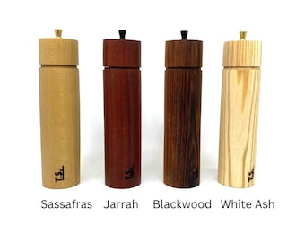 Op de afbeelding: Vier houten pepermolens in verschillende houtsoorten: Sassafras, Jarrah, Blackwood en Witte As. Elke molen heeft een messing bovenkant en een zwarte knop.