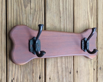 Può includere: Un attaccapanni a parete a forma di osso di cane con due ganci in metallo nero. Il portabiti è realizzato in legno tinto con finitura marrone rossiccio. I ganci sono montati su piastre decorative in metallo nero.