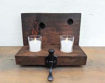 Può includere: Un portacandele rustico in legno marrone scuro con due portacandele in vetro trasparente. Il supporto ha un fermo decorativo in metallo e due fori. Le candele hanno una luce calda e tremolante.