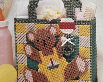 Pode incluir: Uma sacola tote artesanal de tela plástica com um design de urso de pelúcia. A sacola apresenta um padrão xadrez em amarelo, branco e verde. Um urso de pelúcia marrom usando macacão amarelo com um veleiro está na frente. Uma chocalho vermelho e branco está anexado.