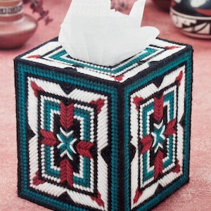 May include: A square tissue box cover with a geometric pattern in teal, red, black, and white. The cover is made of a woven material and has a decorative design on all sides. White tissues are visible at the top.