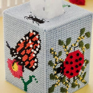 May include: A blue tissue box cover with a butterfly, ladybug, and flowers embroidered on it.
