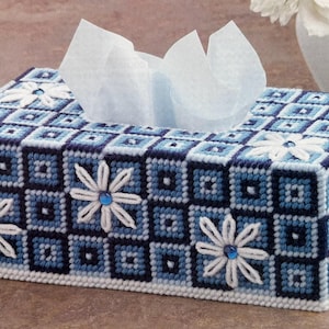 Könnte beinhalten: Ein rechteckiger Taschentuchspender mit einem blau-weißen geometrischen Muster. Der Bezug ist mit weißen, gänseblümchenförmigen Verzierungen mit blauen Zentren versehen. Weiße Taschentücher sind oben sichtbar.