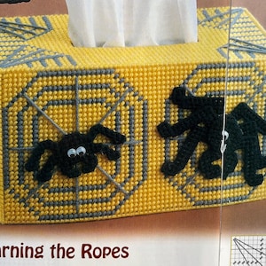 May include: A yellow and grey tissue box cover with a spider web design and black spiders. The text "Learning the Ropes" is printed below the box.