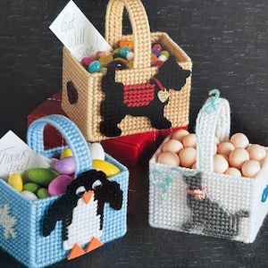 Puede incluir: Tres pequeñas cestas de lona plástica con diferentes diseños. La primera cesta es de color beige con un perro negro y el texto "Made with Love". La segunda cesta es azul con un pingüino. La tercera cesta es blanca con un perro gris. Cada cesta está llena de caramelos de colores.