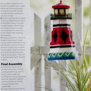 Peut inclure: Un carillon en forme de phare fait à la main, avec un toit rouge, des détails noirs et un corps blanc et rouge. Il est suspendu à une ficelle et comporte un charme en forme d'ancre. Le texte "Lighthouse Wind Bell" est visible.