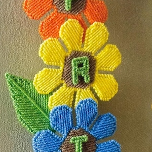 May include: A vibrant, handmade floral wall hanging. Each flower is a different colour, with the letters "PRINTING" stitched in the centre of each flower. The flowers are red, orange, yellow, blue, pink, and purple.