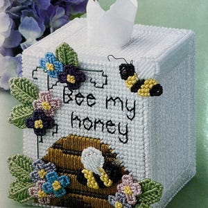 May include: White tissue box cover with a bee and honeycomb design. The cover is decorated with embroidered flowers and leaves. The text "Bee my honey" is embroidered on the front.