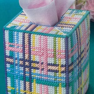 May include: A colorful plaid tissue box cover with a pink, blue, green, yellow, and white pattern. The cover is made of plastic canvas and is perfect for adding a touch of whimsy to any room.