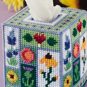 May include: A square tissue box cover with a colorful floral design. The cover is made of plastic canvas and features a variety of flowers, including sunflowers, daisies, and wildflowers. The cover is a great way to add a touch of spring to your home.