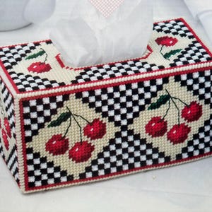 May include: A rectangular tissue box cover with a checkerboard pattern in black and white, accented with red trim. The design features embroidered red cherries with green leaves. White tissues are visible at the top.