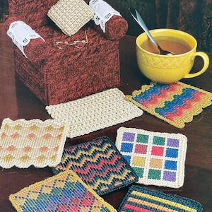 May include: A collection of rectangular and square crochet coasters featuring various geometric patterns in multicolored, solid, and striped designs, alongside a miniature dark red crochet armchair with white lace accents and a yellow mug.