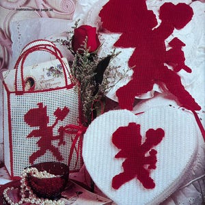 May include: A white heart-shaped box with a red cupid design. A red tote bag with a red cupid design. A red rose with green leaves. A string of white pearls.