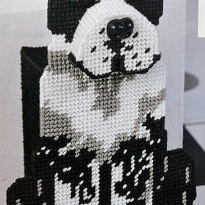 Op de afbeelding: Een zwart-wit gehaakt hondenbeeldje met roze oren en een zwarte neus. De hond zit met een bot in zijn poten. Het bot is gehaakt en heeft de tekst "BONE" erop.