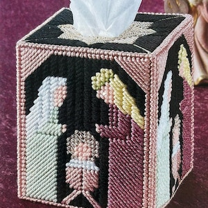 Könnte beinhalten: Ein schwarzer und rosa bestickter Taschentuchbox-Bezug mit einer Weihnachtsgeschichte. Der Bezug zeigt einen Stern, drei Figuren und ein Baby in einer Krippe.