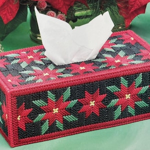 May include: Rectangular tissue box cover with a poinsettia design. The cover is red with black and green accents, featuring red poinsettia flowers and green leaves. White tissues are visible at the top.