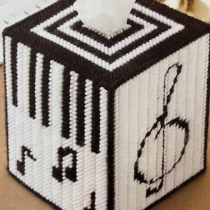 May include: A black and white tissue box cover with a musical note design. The cover is made of yarn and has a 3D effect.