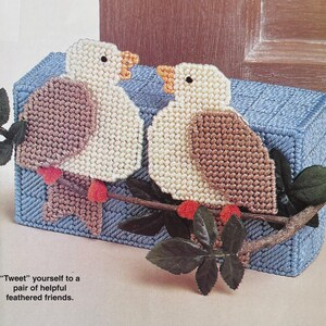 May include: A rectangular blue plastic canvas tissue box cover featuring two cream-coloured birds with brown wings perched on a brown branch with dark green leaves and red berries. The text "Tweet" yourself to a pair of helpful feathered friends is visible.