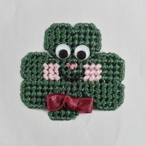 May include: A green felt shamrock with googly eyes and a burgundy bow. The shamrock is a traditional Irish symbol.