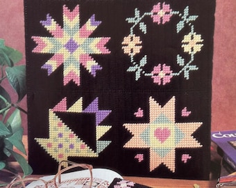 May include: A black tote bag with four colorful cross-stitch designs: a starburst, a floral wreath, a basket, and a star with a heart. The bag contains books. A matching eyeglass case with a floral design rests on an open book.