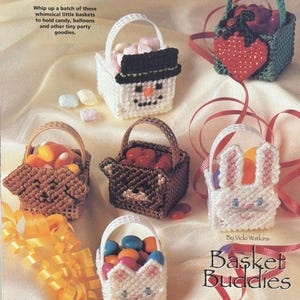 以下が含まれることがあります： 動物や休日のテーマが異なる、カラフルなプラスチック製のキャンバス製のバスケットが6つあります。バスケットはキャンディーで満たされ、リボンで飾られています。画像には「Basket Buddies」というテキストが印刷されています。