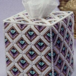 May include: A square tissue box cover with a geometric pattern. The cover is white with a diamond pattern in shades of purple, teal, and gold. White tissues are visible at the top.