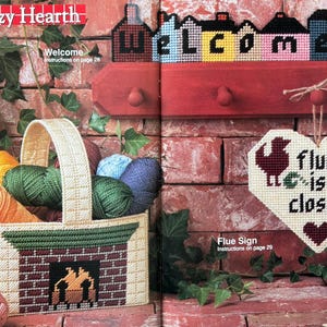 May include: A plastic canvas craft project featuring a basket shaped like a fireplace filled with colourful yarn, a wall-mounted coat rack with a house-shaped sign reading Welcome, and a heart-shaped sign reading Flue is closed with two birds.