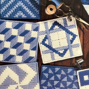 May include: Five different blue and white embroidered squares with geometric patterns. The squares are on a wooden surface with a spool of thread, scissors, and a thimble.