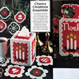 May include: A plastic canvas craft set titled Cheery Christmas Ensemble featuring a tissue box cover, coasters, and a door hanger. The items are stitched with red, white, green, and black yarn in candle, bell, snowflake, and floral patterns.