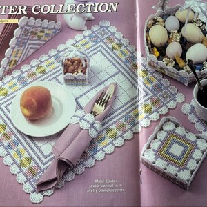 May include: A collection of plastic canvas items including a placemat, napkin holder, basket, and coaster, all featuring a white grid base with pastel yellow, blue, and purple geometric patterns. The set includes a white plate with a peach, a fork, and a mug.