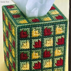 May include: A green, red and yellow tissue box cover with a geometric pattern. The tissue box cover is made of plastic canvas and is decorated with a repeating pattern of squares.