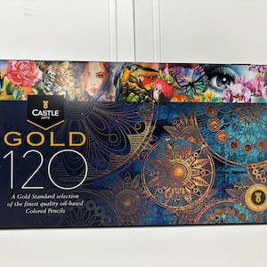 Op de afbeelding: Een rechthoekig metalen blik voor Castle Arts Gold 120 kleurpotloden op oliebasis. Het deksel heeft een donkerblauwe achtergrond met gouden mandalapatronen, een bovenrand met kleurrijke illustraties en de tekst Castle Arts Gold 120.