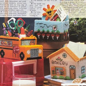 Könnte beinhalten: Drei Kunststoff-Gewebe-Organizer: ein gelber Schulbus-Stiftehalter gefüllt mit Buntstiften und Scheren, eine hellblaue Box mit Gartenthema und Radieschensamen-Tüte sowie ein weißer, hausförmiger Behälter mit der Aufschrift BAKERY für Notizzettel.